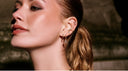 Nahaufnahme einer Frau mit mehreren goldenen Ohrringen und Piercings am Ohr. Eleganter Ohrschmuck mit funkelnden Steinen und modernem Ear Stack in warmem Licht.
